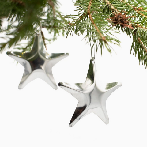 Silver star-shaped Christmas ornaments hanging on a green pine branch.
